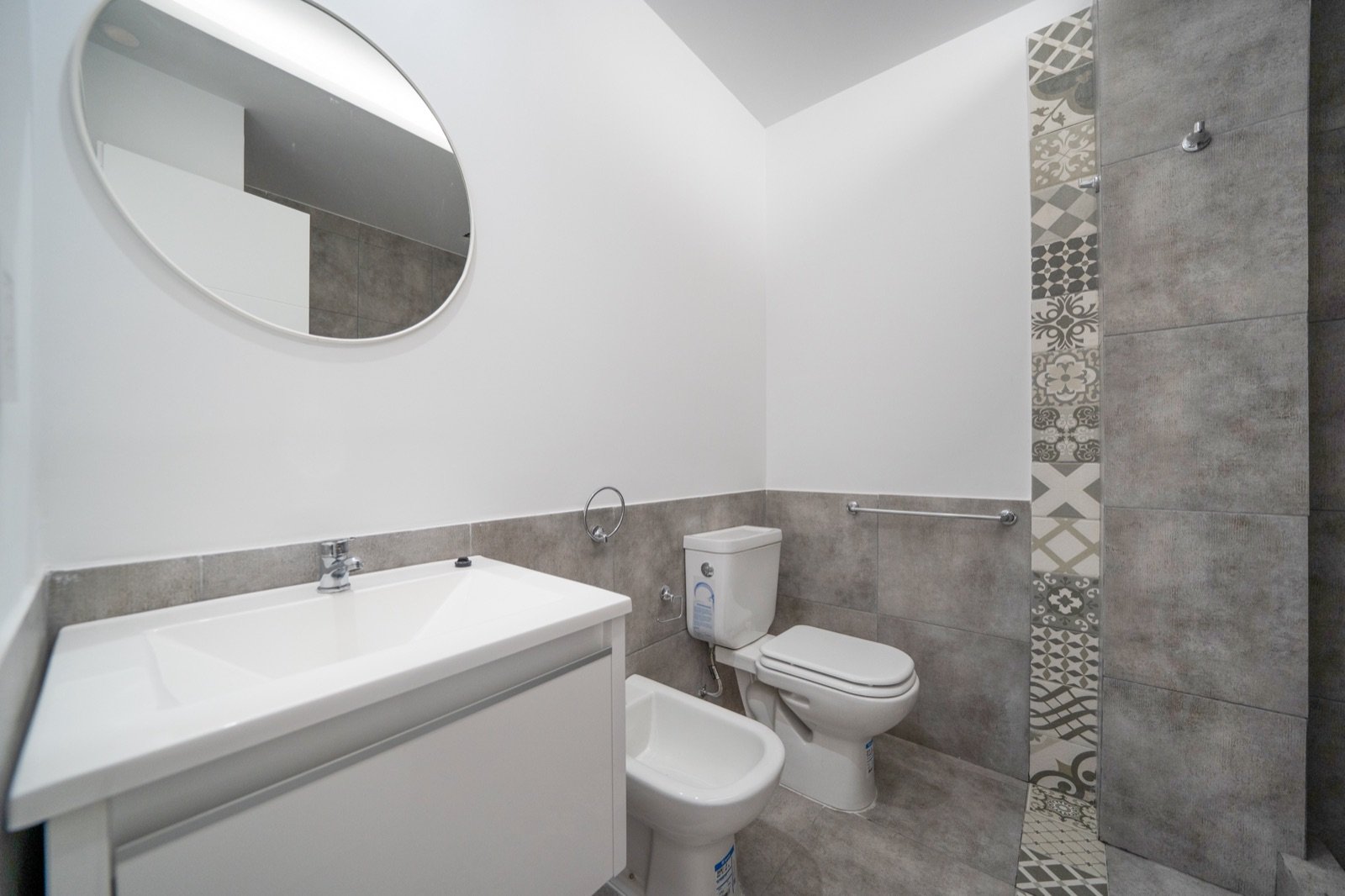 Baño con espejo redondo y ducha revestida